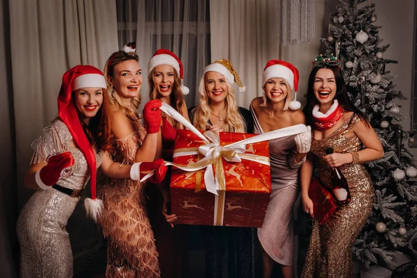 Sexy ženy v Santa klobouky s sklenicemi šampaňského a velkým dárkem. Novoroční prázdniny. Štědrý večer. Na pozadí interiéru domu. Šťastný nový rok — Stock fotografie