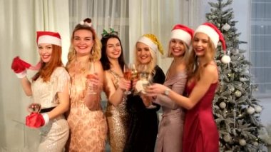 Şampanya bardaklı, dans eden ve gülen Noel Baba şapkalı seksi kadınlar. Yeni yıl tatili. Mutlu yıllar.