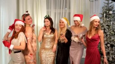 Şampanya kadehleri ve büyük bir hediyeyle Noel Baba şapkalı seksi kadınlar. Yeni yıl tatili. Noel arifesi. Evin arka planında var. Mutlu yıllar..