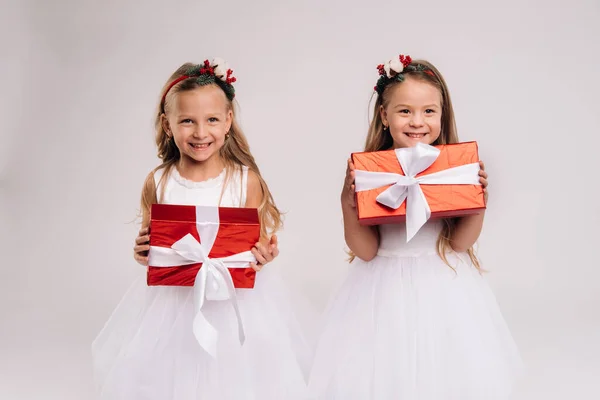 两个身穿白色礼服 背景为白色笑容的小女孩 带着圣诞礼物 — 图库照片