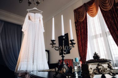 Ahşap bir askıda asılı eski bir gelinlik ve kaledeki bir masada duran bir mum tutacağı..