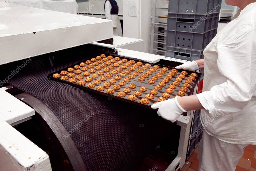 A tray of ready-made cookies is taken from the conveyor belt in the bakery.