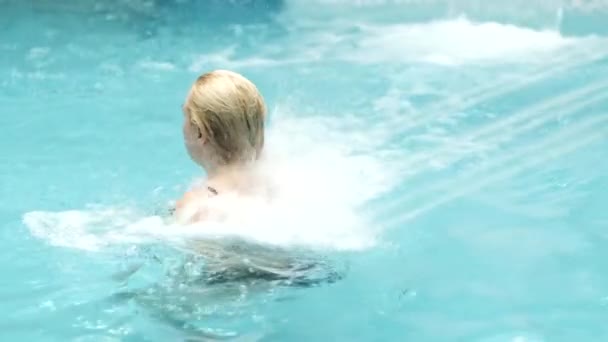 Dziewczyna w kostiumie kąpielowym jest oblana strumieniem wody w basenie parku wodnego — Wideo stockowe