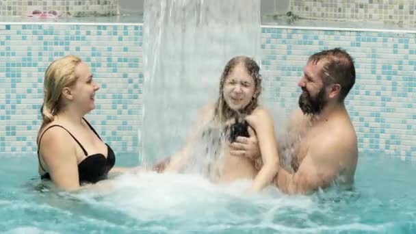 Trzyosobowa rodzina pod wodospadem z strumieniem wody w niebieskim basenie. — Wideo stockowe