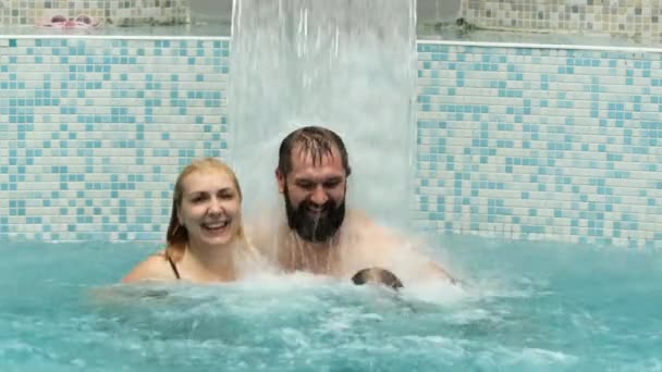 Paar Mann und Frau unter einem Wasserfall mit dem Strom des Wassers in blauen Pool — Stockvideo