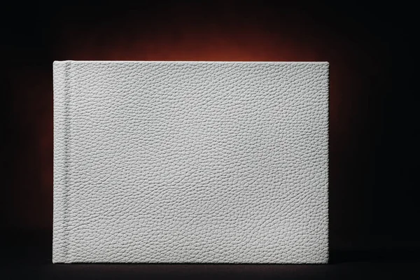 White book in genuine white leather on a dark embossed background . White paper on a dark background