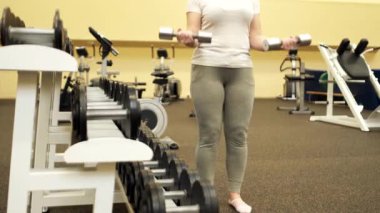 Kız ellerinin arasında dambıl tutuyor ve spor salonunda egzersiz yapıyor..