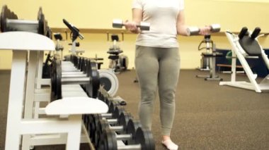 Kız ellerinin arasında dambıl tutuyor ve spor salonunda egzersiz yapıyor..
