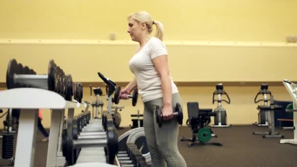 La chica pone las mancuernas en su lugar en el gimnasio después de un entrenamiento — Vídeos de Stock