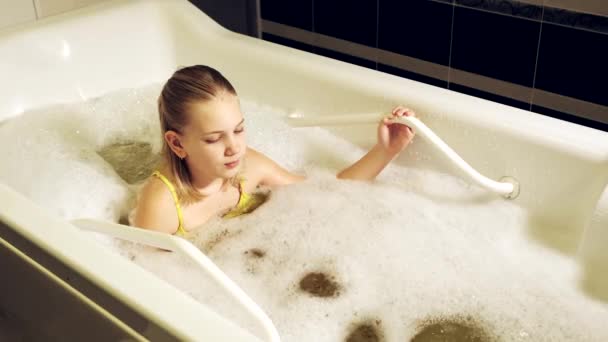 Una niña pequeña toma el procedimiento en un baño mineral. El paciente recibe tratamientos de agua con un baño de perlas minerales. — Vídeo de stock
