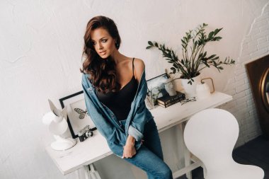 Uzun saçlı bir esmer masanın içinde poz veriyor..