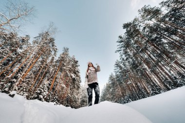 Süveter giyen ve kışın eldiven giyen bir kız karla kaplı bir arka planda duruyor..