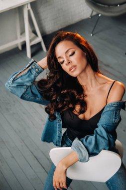 Uzun saçlı esmer bir kız stüdyoda bir sandalyede oturuyor..