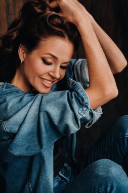 Uzun saçlı bir esmer, stüdyoda siyah bir arka planda, yerde oturuyor..