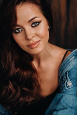 Uzun saçlı bir esmer, stüdyoda siyah bir arka planda, yerde oturuyor..