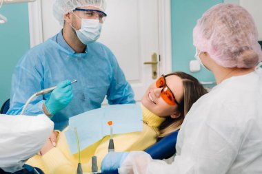 Hasta diş hekiminin sandalyesinde koruyucu maske ve aletle gülümsüyor.