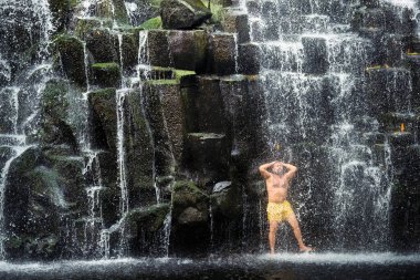 Ormanda bir adam şelalenin altında duruyor. Mağara şelalesinde bir adam..