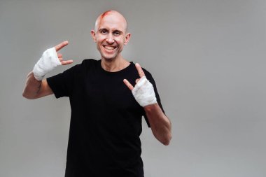 Gri bir arka planda siyah tişörtlü hırpalanmış bir adam duruyor.