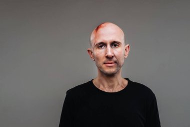 Uyuşturucu bağımlısı gibi görünen siyah tişörtlü hırpalanmış bir adam ve gri bir arka planda duran bir ayyaş.