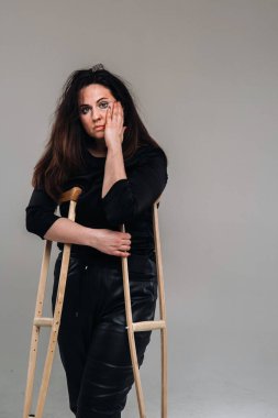 Siyah elbiseli, elleri alçılı, gri arka planda hırpalanmış bir kadın.