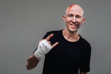 Gri bir arka planda siyah tişörtlü hırpalanmış bir adam duruyor..