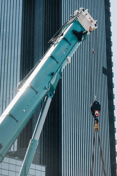 blue crane lifting mechanism with hooks near the glass modern building, crane and hydraulic high lift up to 120 meters.