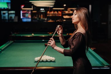 Elbiseli bir kız elinde ıstakayla elinde tebeşirle elinde toplarıyla bilardo oynuyor. Bilardo oynuyor..