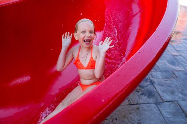 Pembe mayo giymiş küçük bir kız yaz tatillerinde su kaydırağından kayıyor. Yunanistan.