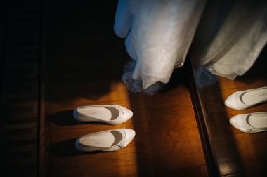 Beyaz düğün ayakkabıları sahanın üzerinde duruyor. Elbisenin yanında..