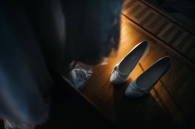 Beyaz düğün ayakkabıları sahanın üzerinde duruyor. Elbisenin yanında..