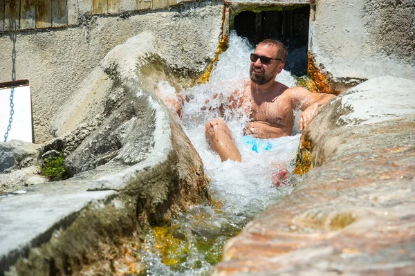 Un hombre con gafas se sienta bajo una cascada de agua sanadora con manantiales termales en Pamukkale.Turquía — Foto de Stock