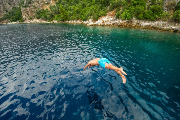 Un hombre en pantalones cortos azules se sumerge desde un barco en el mar cerca de la orilla — Foto de Stock