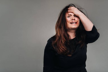 Siyah elbiseli hırpalanmış bir kadın kafasını izole edilmiş gri arka planda tutuyor. Kadınlara şiddet.