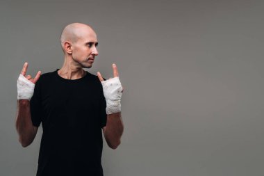 Eli siyah bir tişörte sarılı, gri bir arka planda uyuşturucu bağımlısı ve ayyaş gibi görünen hırpalanmış bir adam..