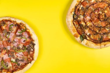 Sarı arka planda iki farklı lezzetli büyük pizza.