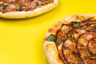 Sarı arka planda iki farklı lezzetli büyük pizza.