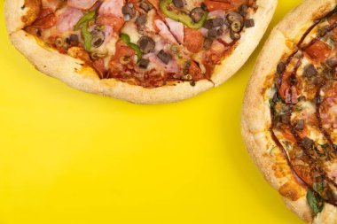 Sarı arka planda iki farklı lezzetli büyük pizza.