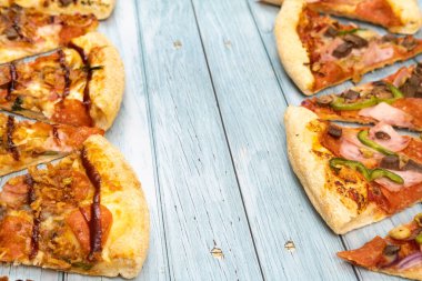 Mavi ahşap arka planda bir sürü lezzetli üçgen pizza dilimleri var.