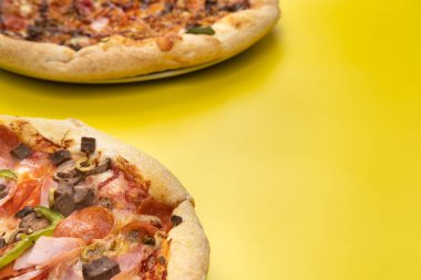 Sarı arka planda iki farklı lezzetli büyük pizza..