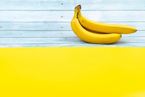 Gele bananen liggen op een blauwe houten achtergrond en een gele achtergrond — Stockfoto