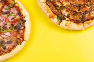 Sarı arka planda iki farklı lezzetli büyük pizza.