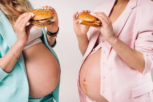 Dvě Těhotné Ženy Oblecích Hamburgery Rukou Šedém Pozadí — Stock fotografie
