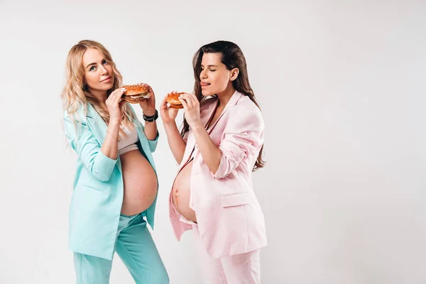 Duas Mulheres Grávidas Ternos Com Hambúrgueres Suas Mãos Fundo Cinza — Fotografia de Stock