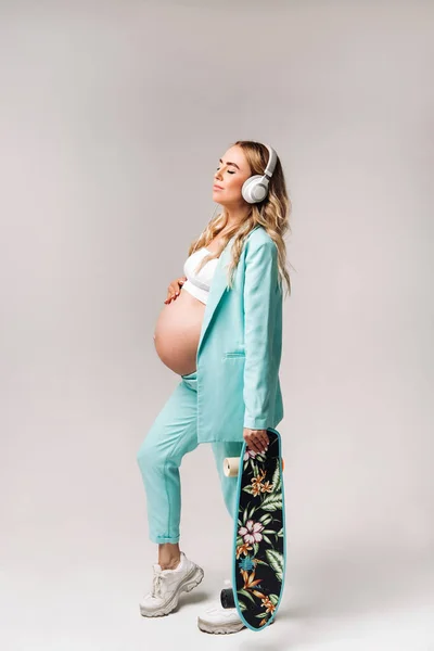 Pregnant Girl Turquoise Suit Skateboard Her Hands Headphones Stands Gray — Stock Photo, Image