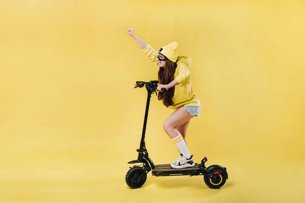 Een zwanger meisje in gele kleren op een elektrische scooter op een geïsoleerde gele achtergrond — Stockfoto