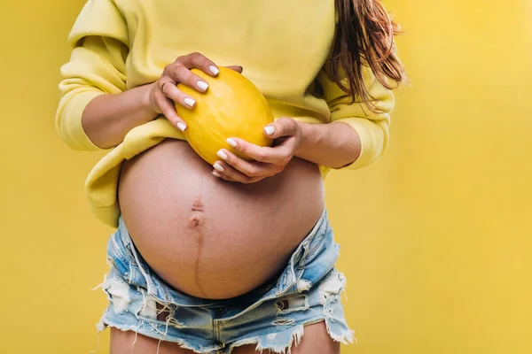 一个穿着黄色夹克的怀孕女孩站在那里，手里拿着一个黄色孤立的背景的甜瓜 — 图库照片