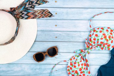 Mavi ahşap bir arka planda duran, gözlüklü, beyaz şapkalı ve mayosu olan saman rengi bir adam..