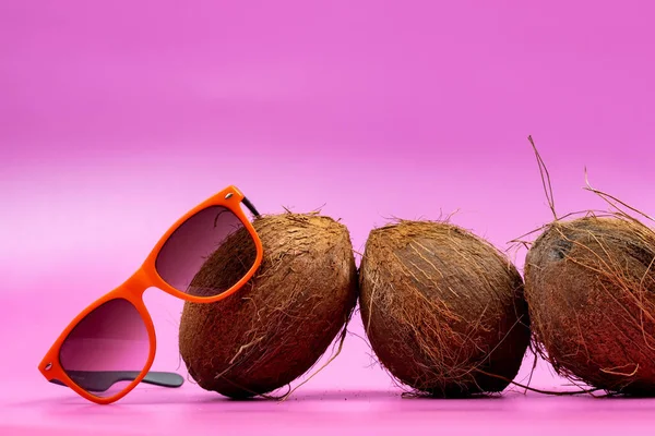 Drei Ganze Kokosnüsse Und Orangefarbene Gläser Auf Rosa Hintergrund — Stockfoto
