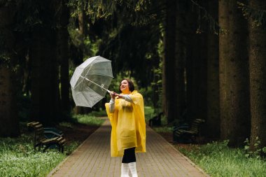 Sarı yağmurluk ve şemsiyeli bir kadın yazın parkta ve bahçede yürür..