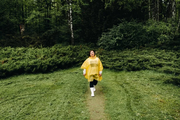 a woman in a yellow raincoat walks in the park in the summer after the rain.